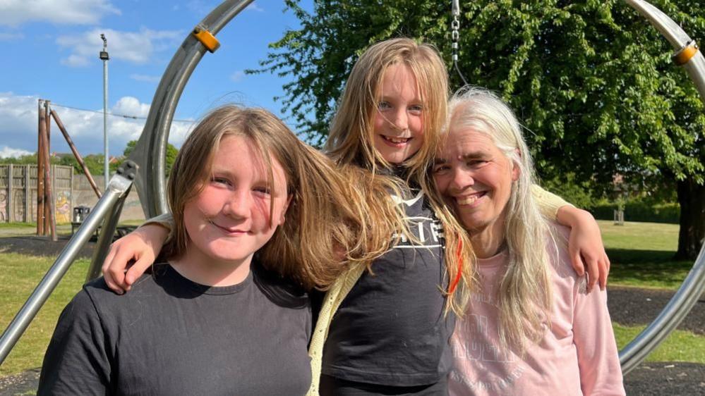 Kaidee, Kairah, and Denise stood in the King George V Recreation Ground, smiling together at the camera.
