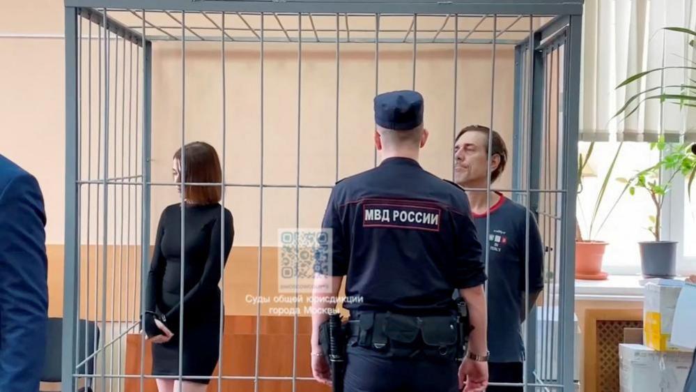 Russian citizen Veronika Grabanchuk and U.S. citizen Michael Travis Leake, accused of drug smuggling, stand inside an enclosure for defendants as they attend a court hearing in Moscow, Russia, on 18 July