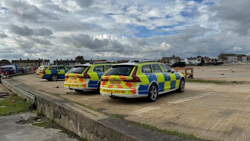 Several police cars are parked up on the Atlas Terminal of Great Yarmouth's river port. Houses can be seen on the far side of the river, which is Southtown Road.