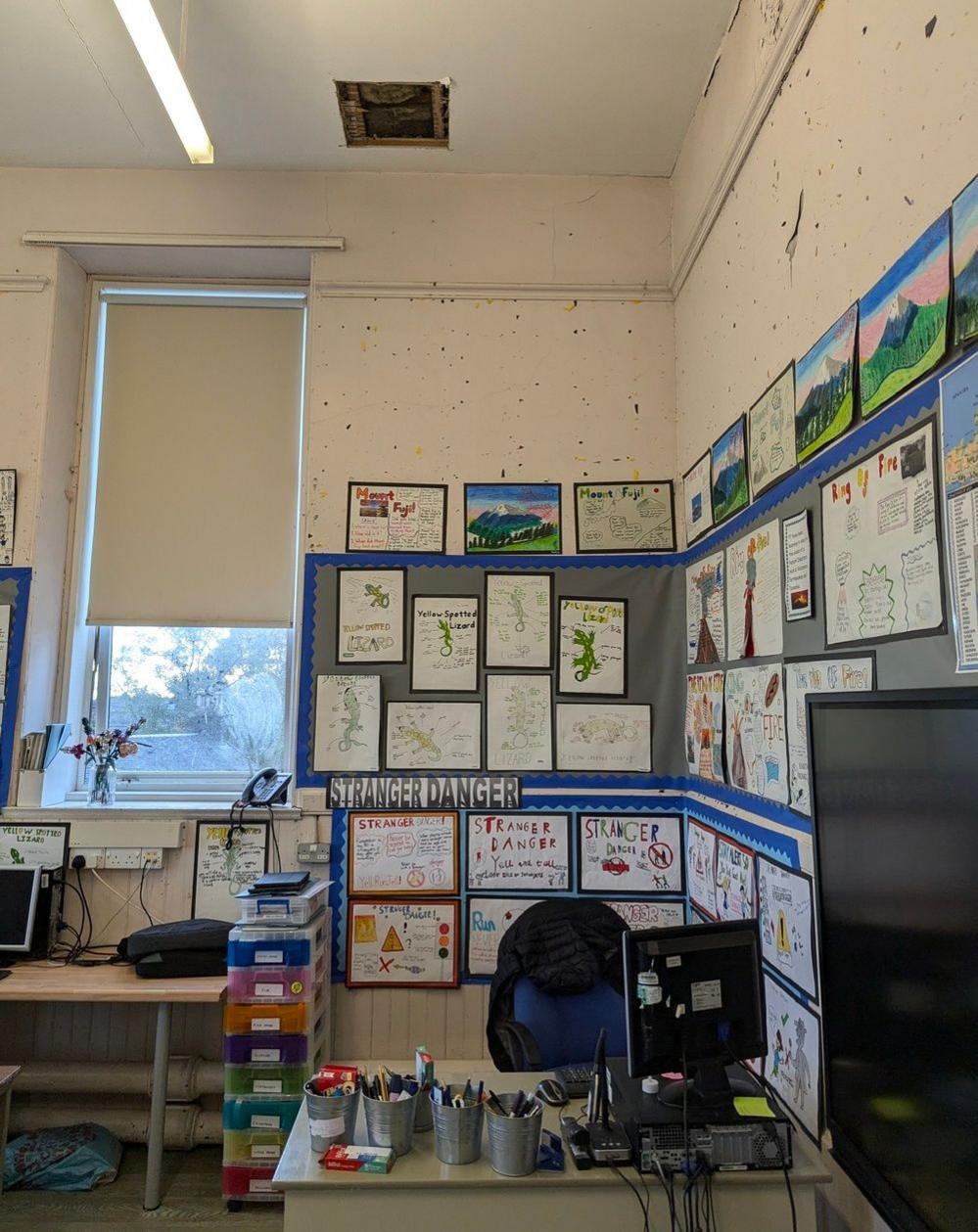 A square shaped hole in the ceiling can be seen where the square of wood fell above the teacher's desk.