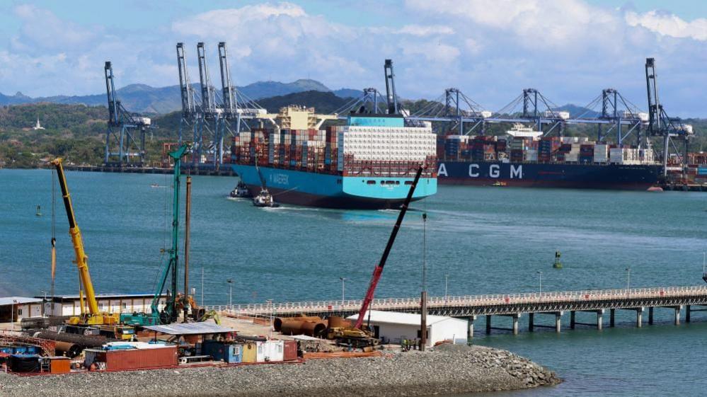 A teal coloured ship being towed into port