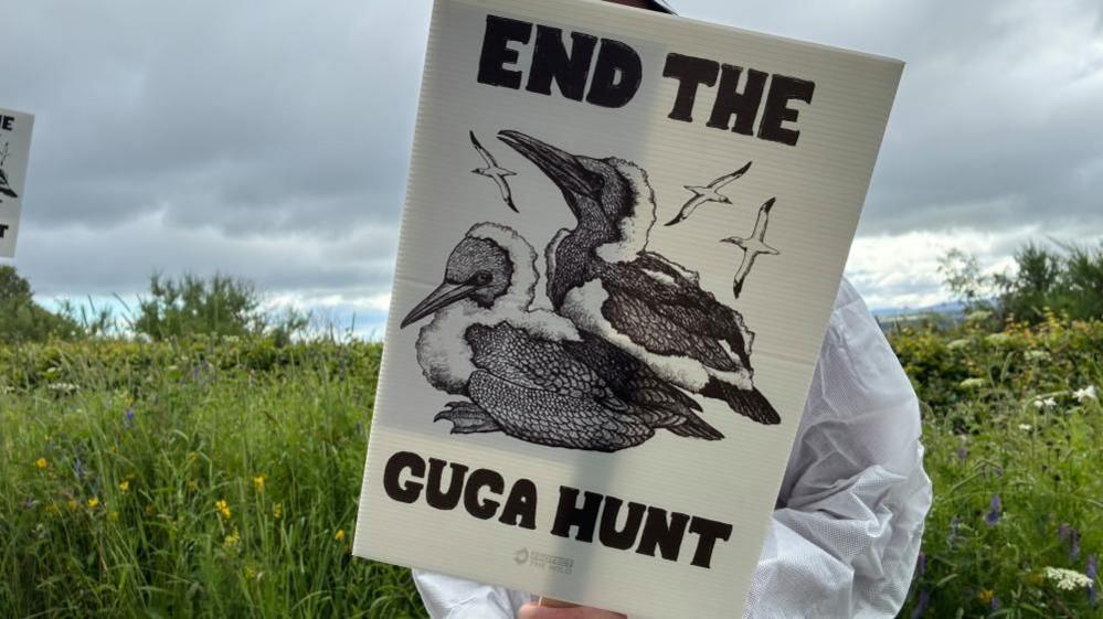 Neach-iomairt nan seasamh le soidhne gam falach. The "End the Guga Hunt" sgrìobhte air an t-soidhne.