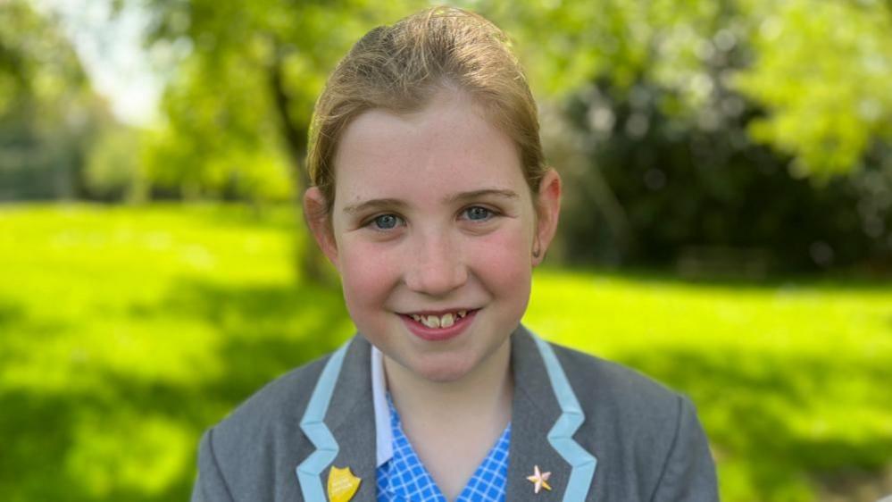 Alice - girl with brown hair tied back wearing grey uniform