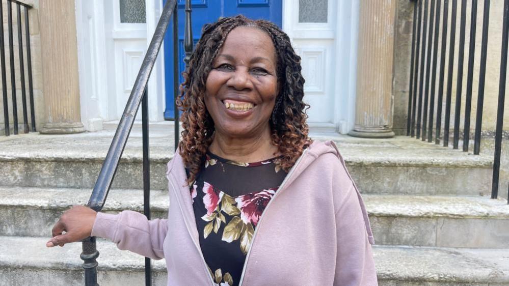 Lilian Francis holding a handrail, wearing a purple hoodie and smiling