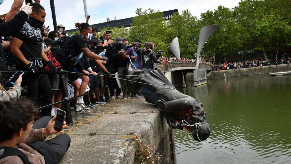 Colston statue being thrown into the harbour with a large crowd in the background