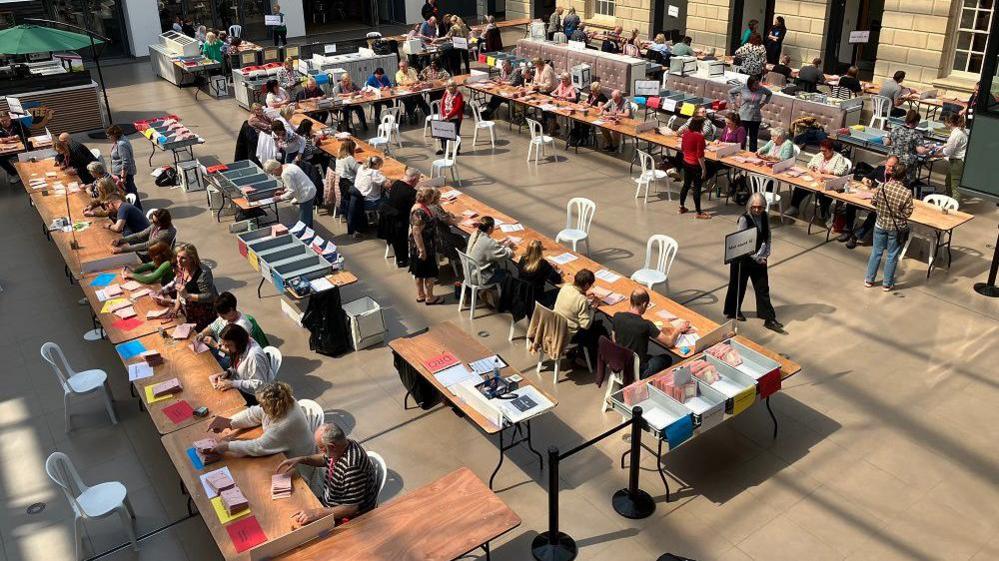 View from above of people sitting at tables counting ballot papers