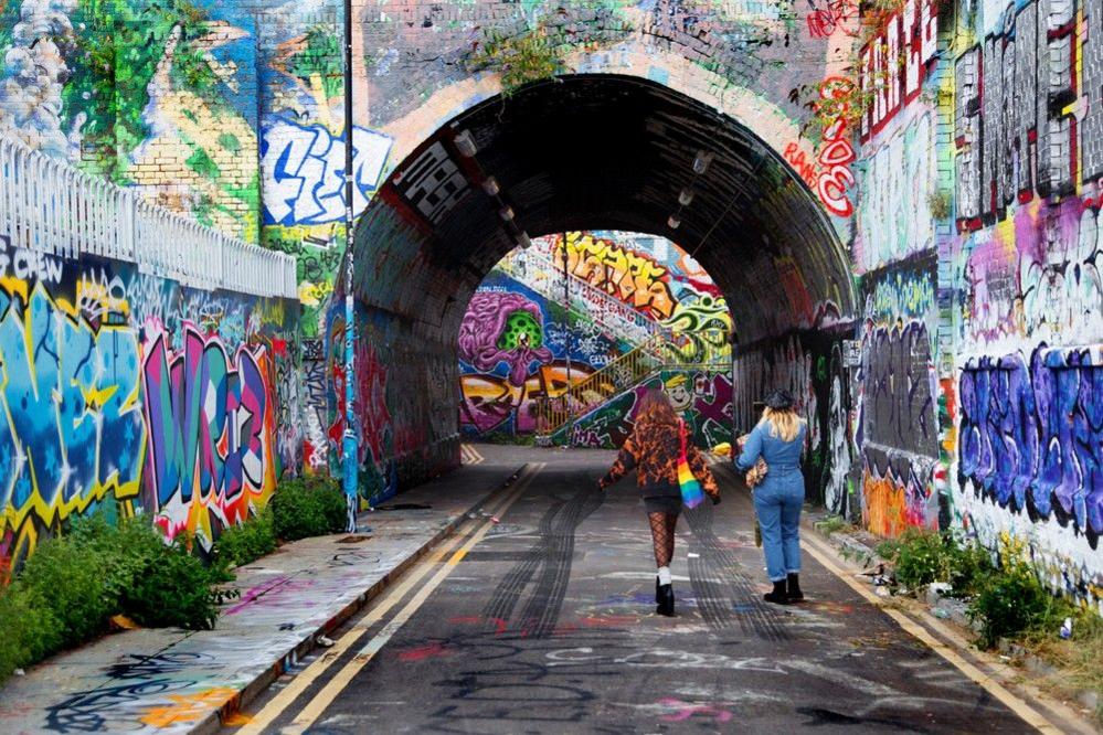 Two people walk towards a railway arch covered in graffiti in London