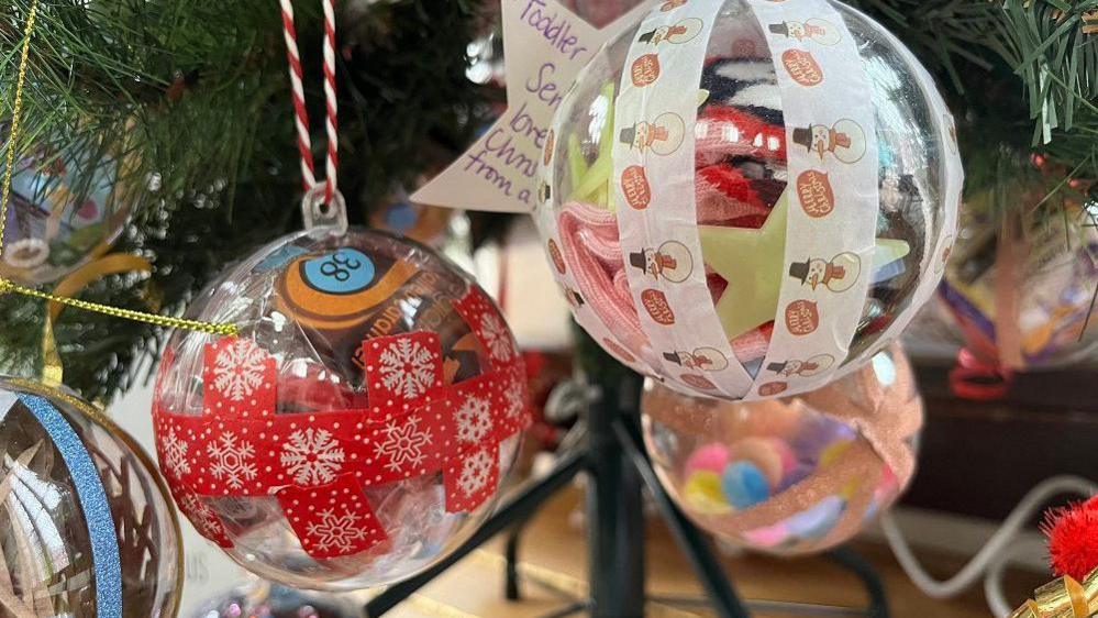 Clear Christmas baubles with red and white tape on them hanging from a Christmas tree branch