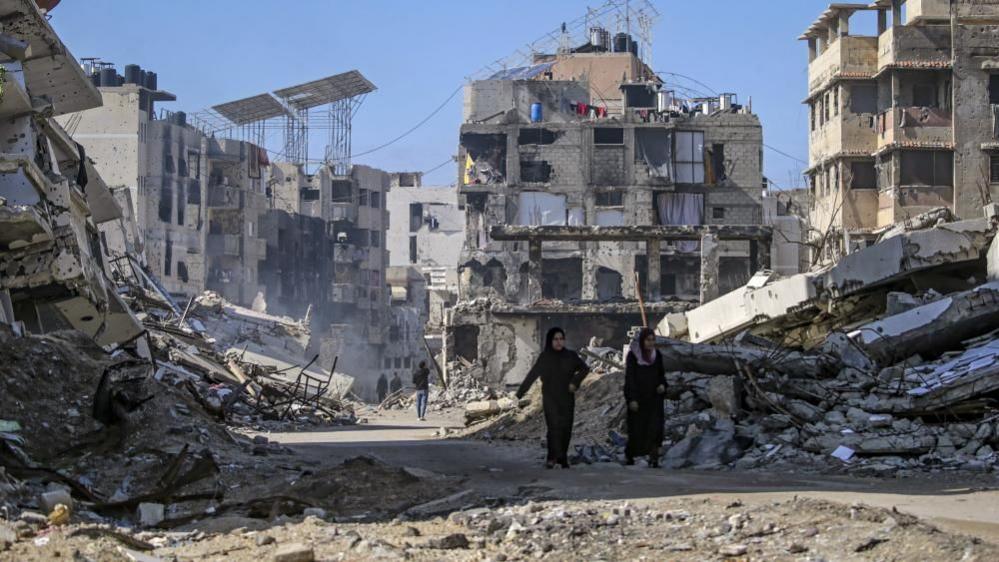 Palestinian women walk between destroyed buildings in Gaza City. Photo: 14 February 2025