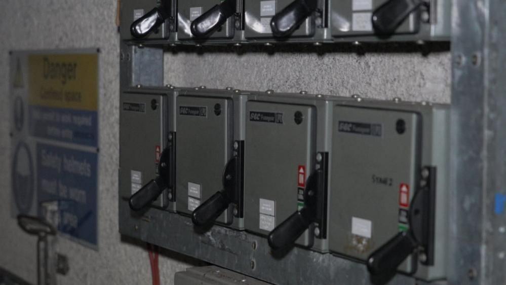 A row of four knife switches inside grey boxes, set within a control panel.