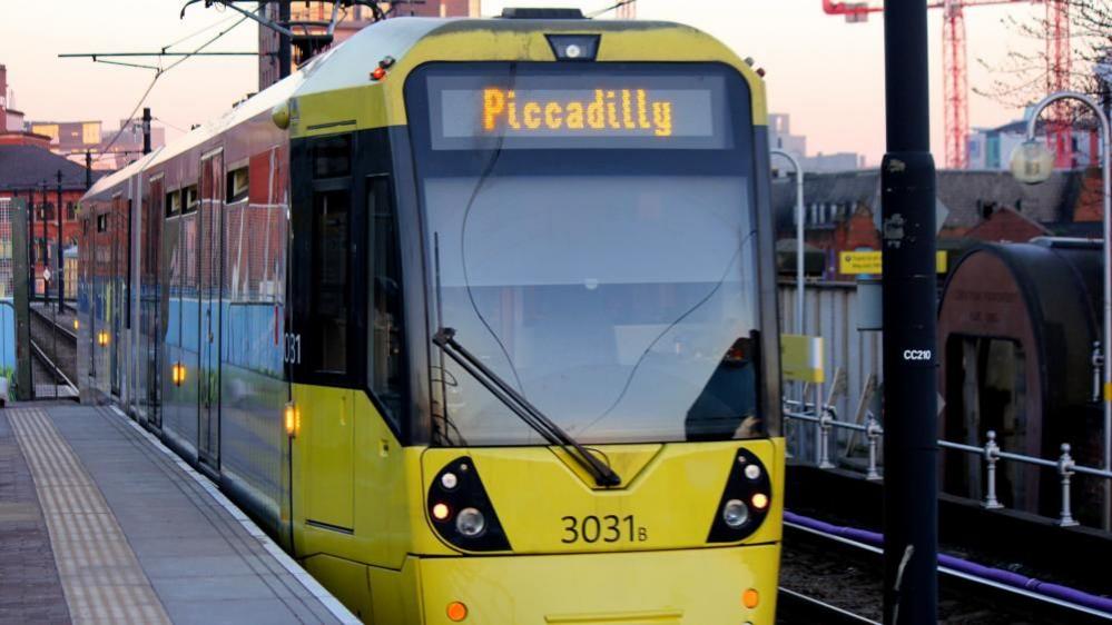 The front of a yellow Manchester Metrolink tram with 'Piccadilly' lit up on the front. 