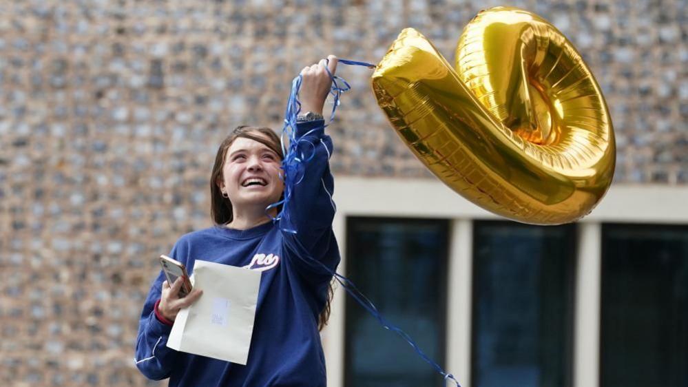 A pupil at Brighton College celebrates achieving nine GCSEs with a balloon. 