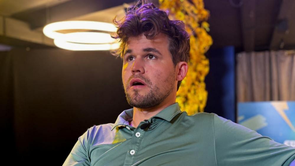A man wearing a green shirt looks into the distance with his mouth open.