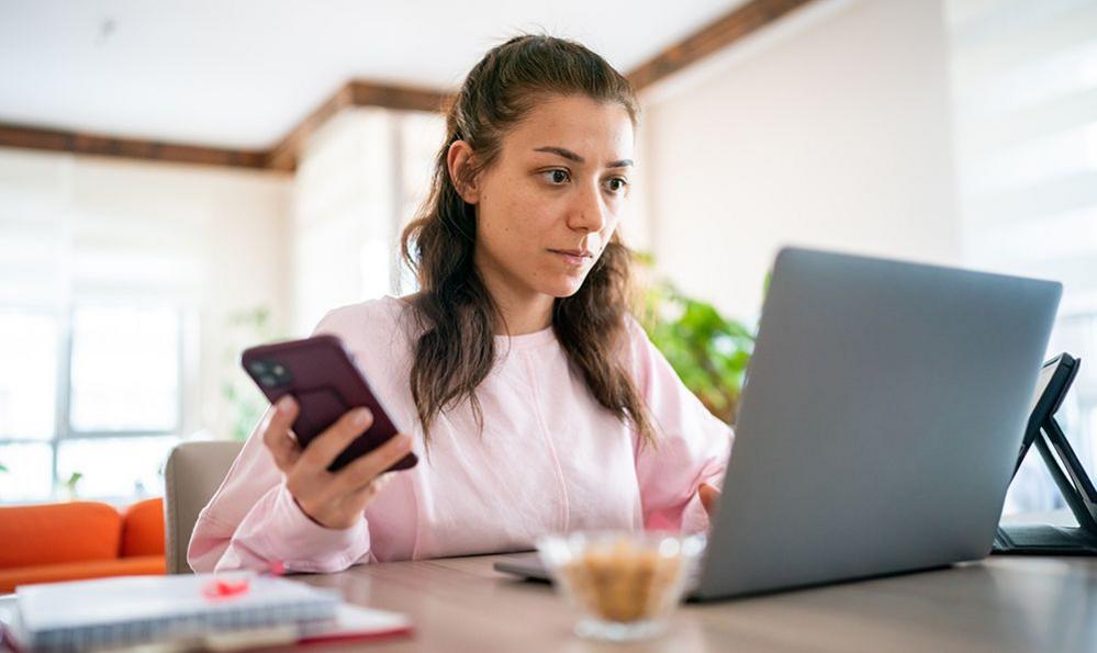 A woman checking her laptop and phone inside at home