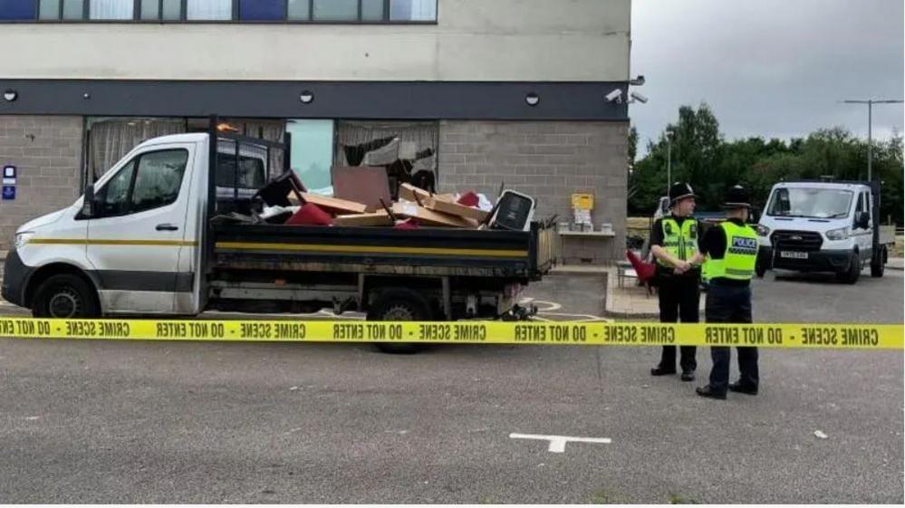 Clean-up operation at the Holiday Inn Express at Manvers, Rotherham, in August, with two police officers standing guard to the right of the image and yellow "crime scene do not enter" police tape around the area.