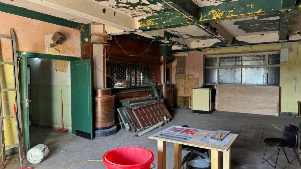 The interior of the Iron Duke, showing some builders' materials and doors stacked against the bar. Paint has peeled from the ceilings.