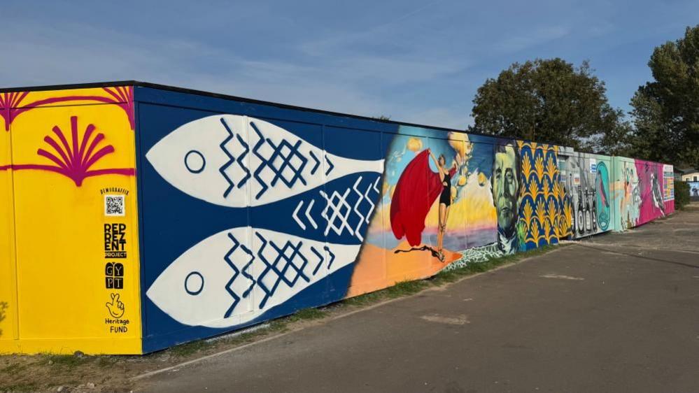 The hoarding in its entirety, featuring two white fish looking left, and a third fish between them pointing right. Other images captured above appear along the remainder of the hoarding.