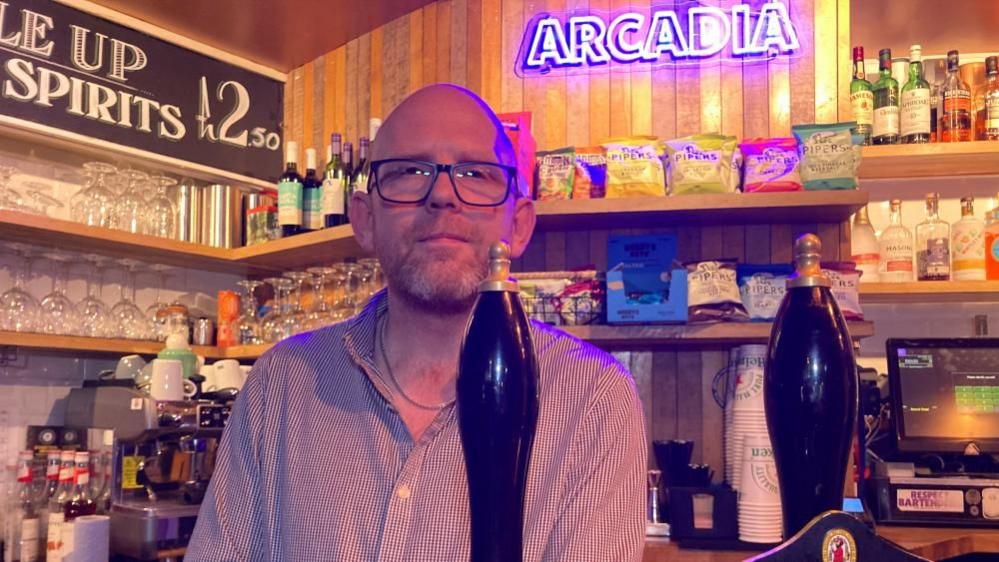 A man stood behind a bar ready to serve customers