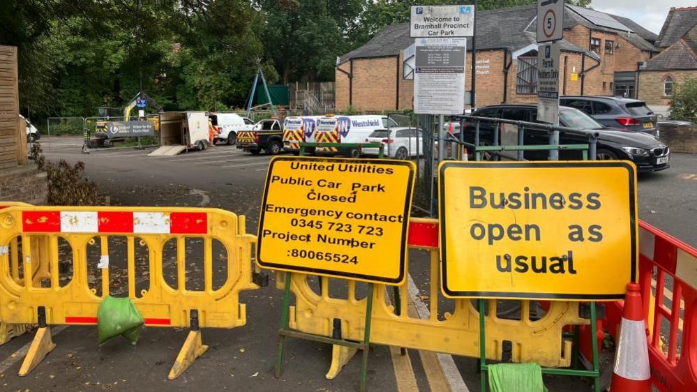 Two yellow signs in front of traffic cones blocking a road. 