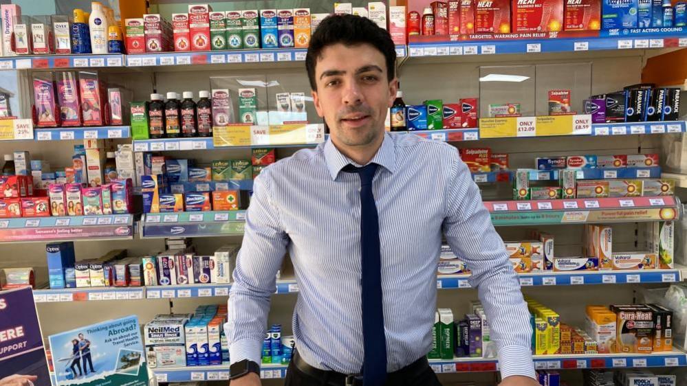 A male pharmacist in front of a range of different medication.