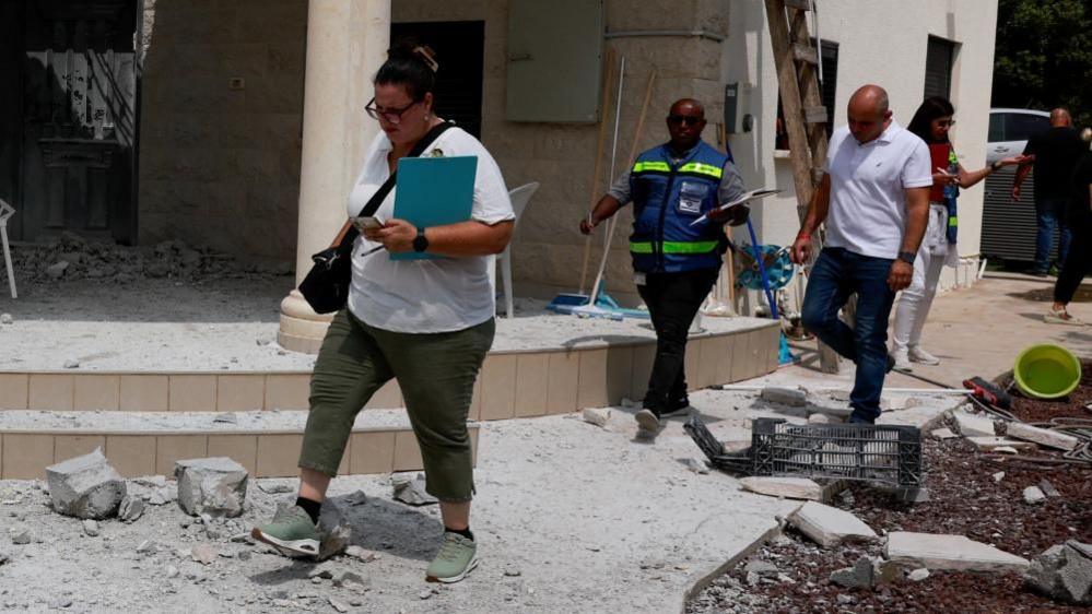 People walk near a damaged building in northern Israel after Hezbollah launched hundreds of rockets and drones towards Israel(25/08/24)