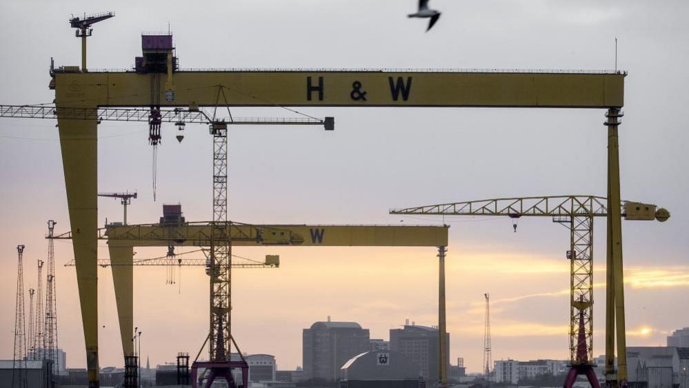 A wide shot of two yellow ship building cranes with the letters H&W in back bold writing.