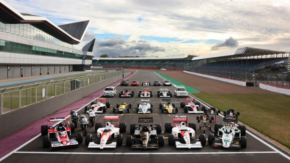 Several race cars of differing vintage lined up on the Silverstone starting grid.