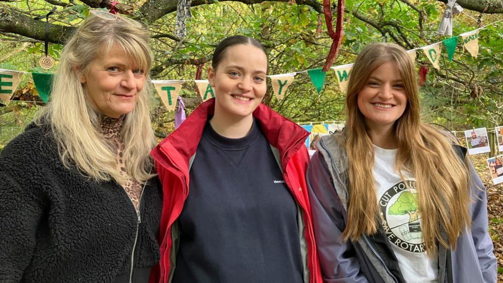 Lily Stockburn (centre) with grandmother Tracey Hardisty and mother Rowan Hardisty. The trio stand in woodland, smiling at the camera. Tracey has blonde hair and wears a black fleece, Lily has dark hair up, a navy sweater and pink waterproof coat and Rowan has long, brown hair and wears a purple waterproof coat.