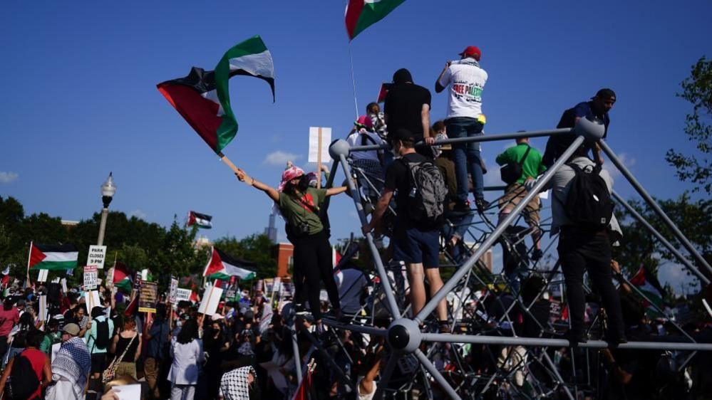 A group of demonstrators waving Palestinian flags climb on a structure