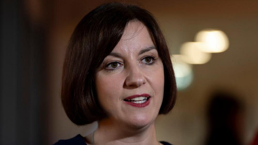 Bridget Phillipson has a dark brown bob hair do as she speaks to members of the press with a neutral expression