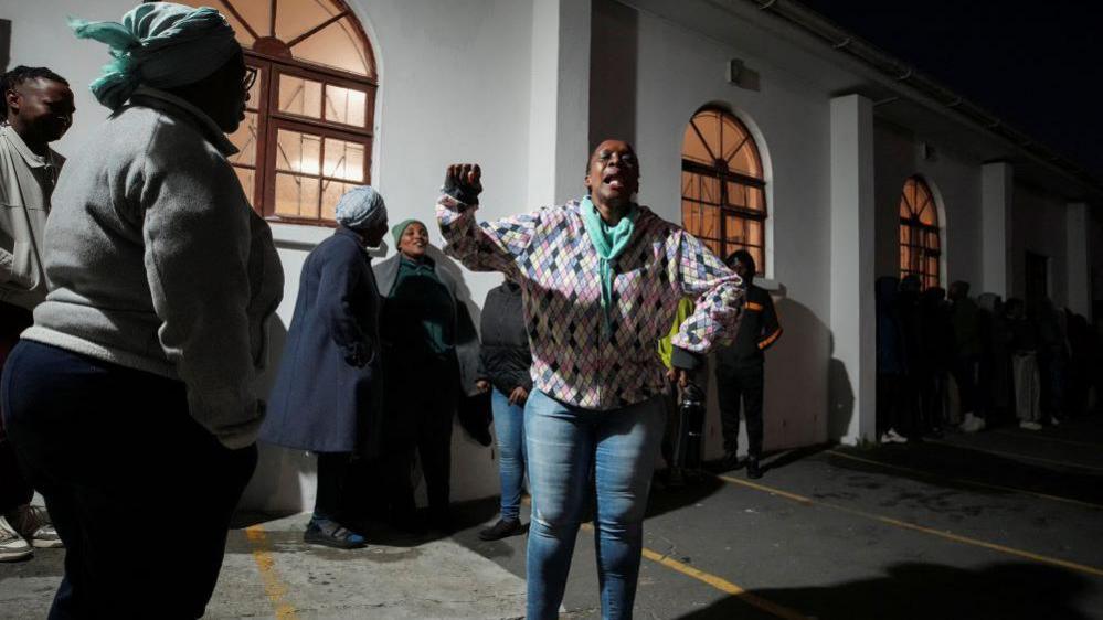 A woman dances as people queue to vote in the South African elections in Masiphumelele, South Africa, May 29, 2024.