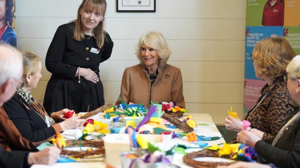 The Queen sits at the head of a long table with people making spring wreaths