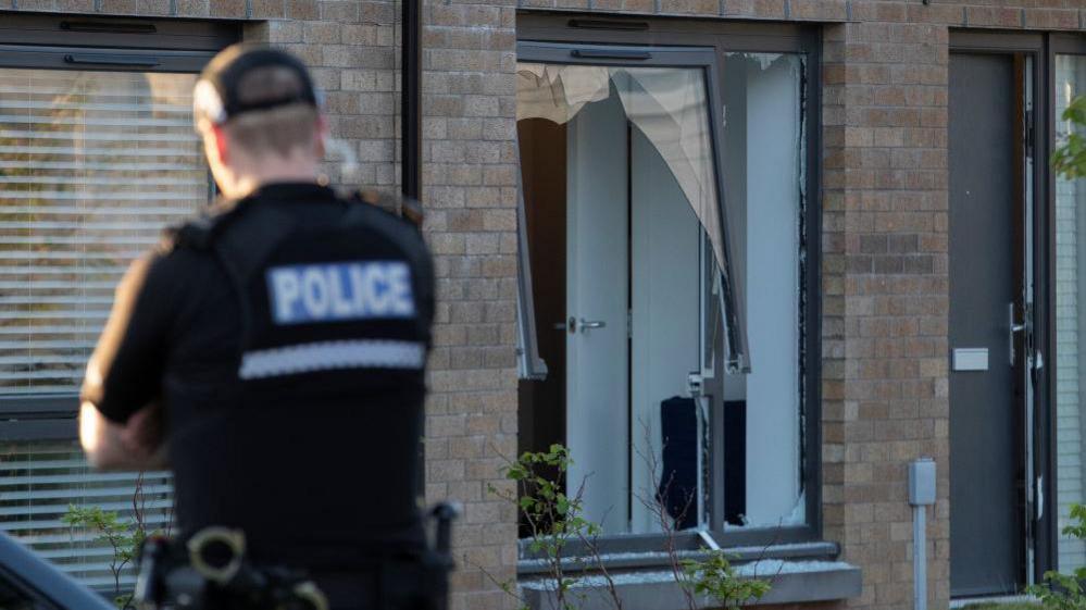 A broken window with a police officer standing in front of it.