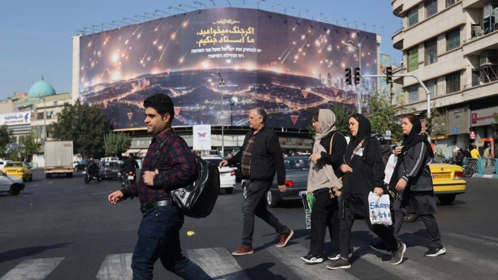 Iranians walk next to an anti-Israel billboard on a street after several explosions were heard, in Tehran, Iran, October 26