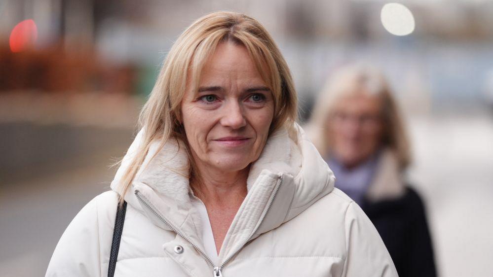 A woman with blonde hair wearing a white puffa jacket.