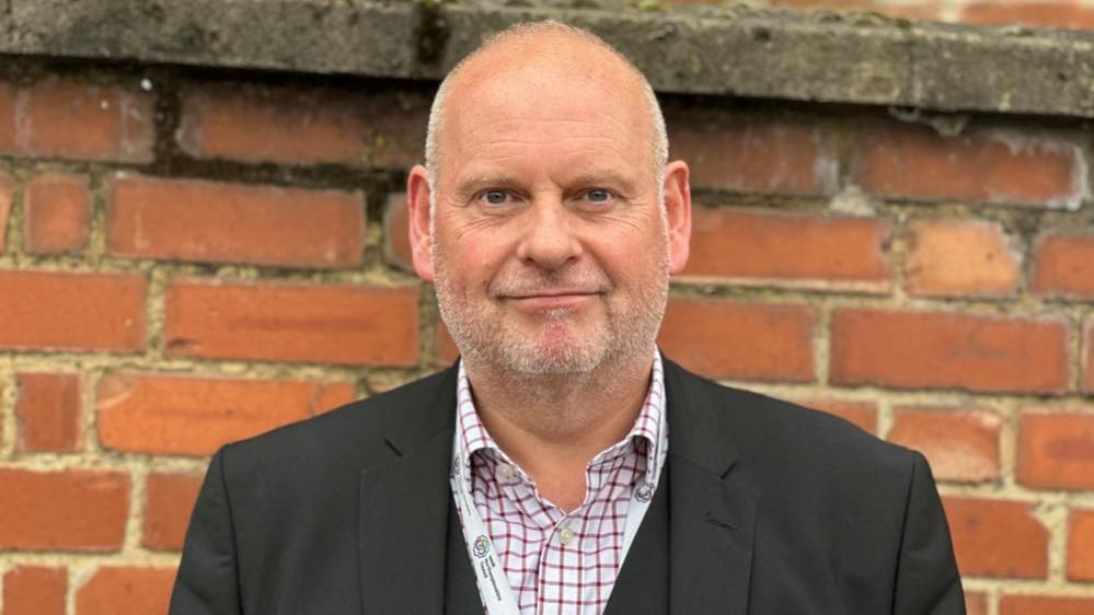 Jonathan Nunn with short hair and beard, standing in front of a brick wall