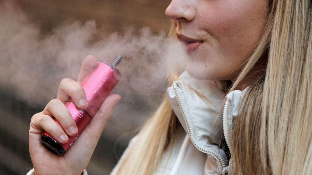 A woman using a pink single-use vaping product