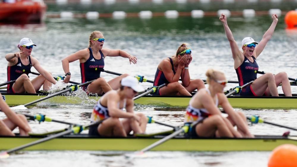 Four athletes react with shock and jubilation, while another team in the foreground are more subdued