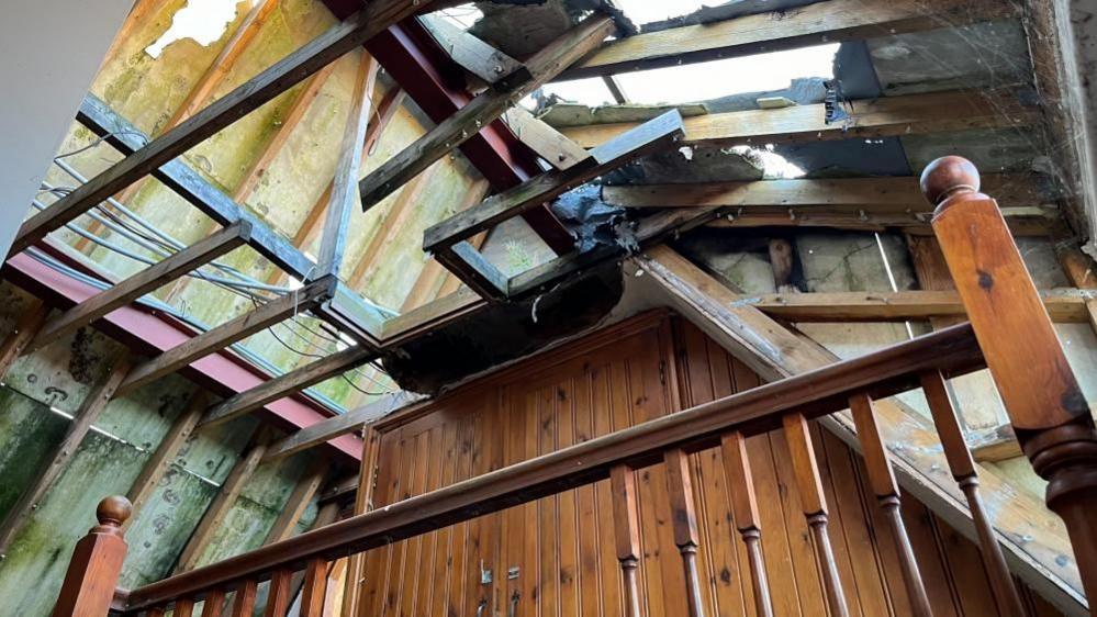 The bare beams and roof area with daylight visible through the holes, burned through in the fire in 2021.