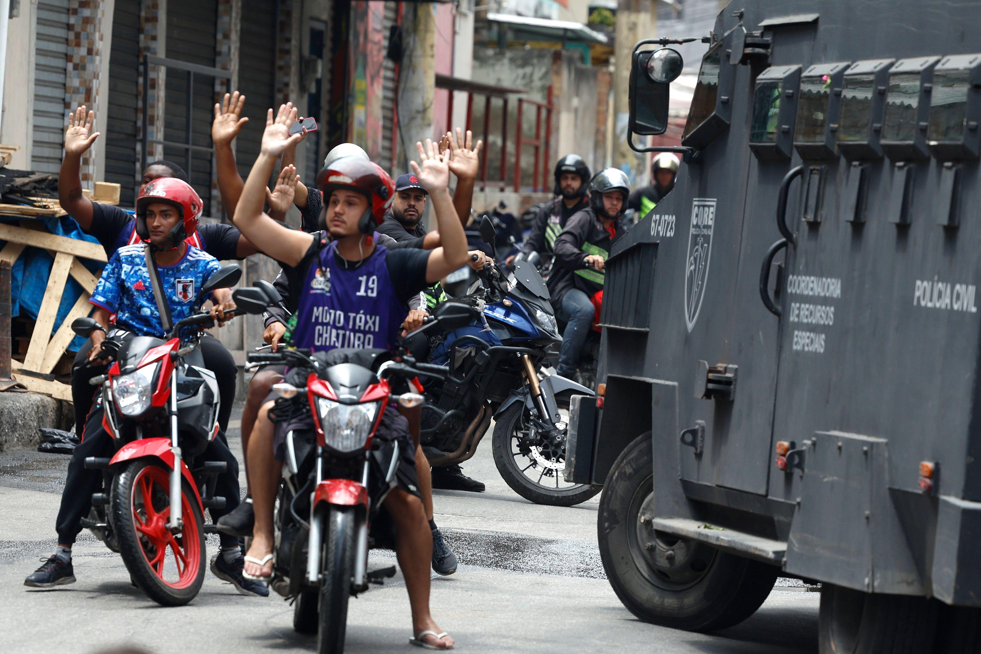 Motociclistas con las manos levantadas al lado de un camión de la policía.