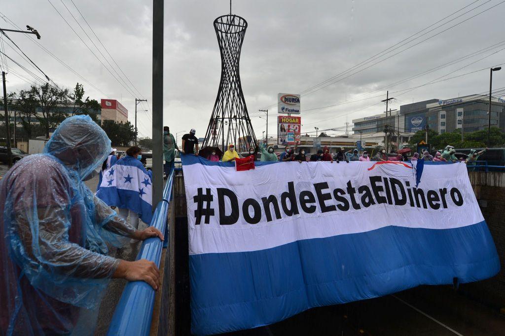 Un grupo de personas sostiene un enorme cartel que dice: ¿Dónde está el dinero?, en el cual tiene los colores de la bandera de Honduras.