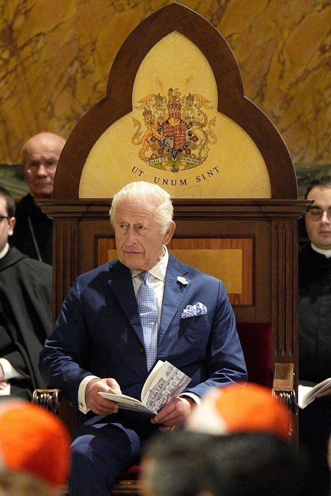 El rey Carlos III sentado en una silla con un pequeño libro en las manos. En la cabecera de la silla está inscrita la frase: "Ut unum sint"