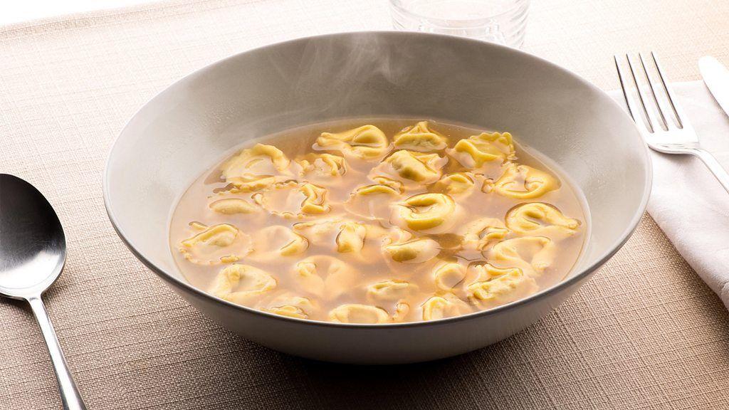 Tazón tortellini in brodo con cubiertos y una servilleta doblada al lado.