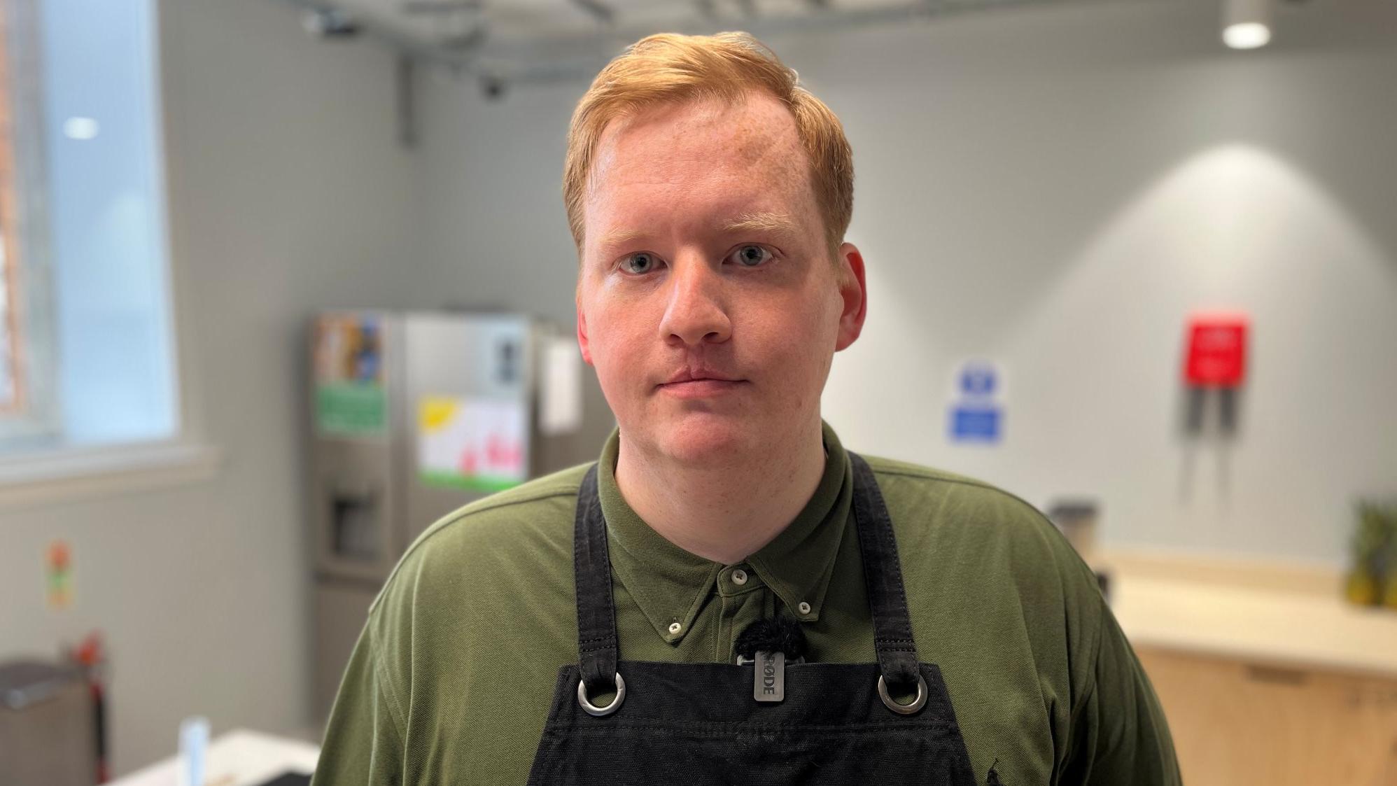 يقف بيتر غيلكريست، داخل مطبخ مرتدياً قميصاً أخضر ومريلة سوداء.