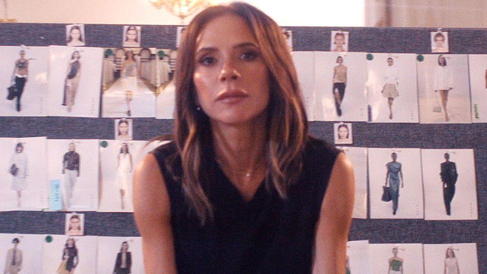 Victoria Beckham em frente a um quadro repleto de fotografias de vestidos, no seu document&aacute;rio na Netflix