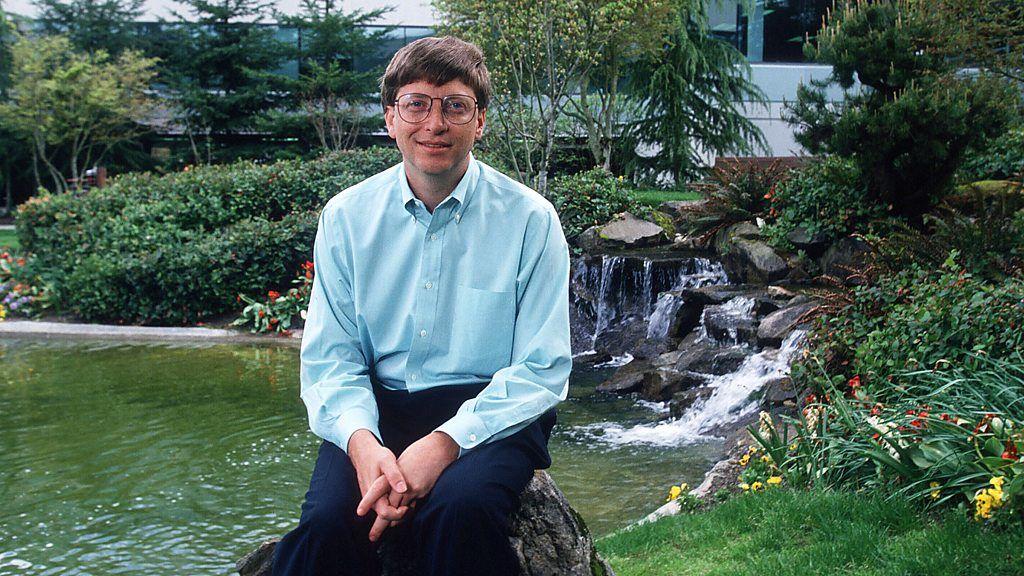 Bill Gates jovem, sentado sobre uma pedra em frente a uma pequena cascata e lago