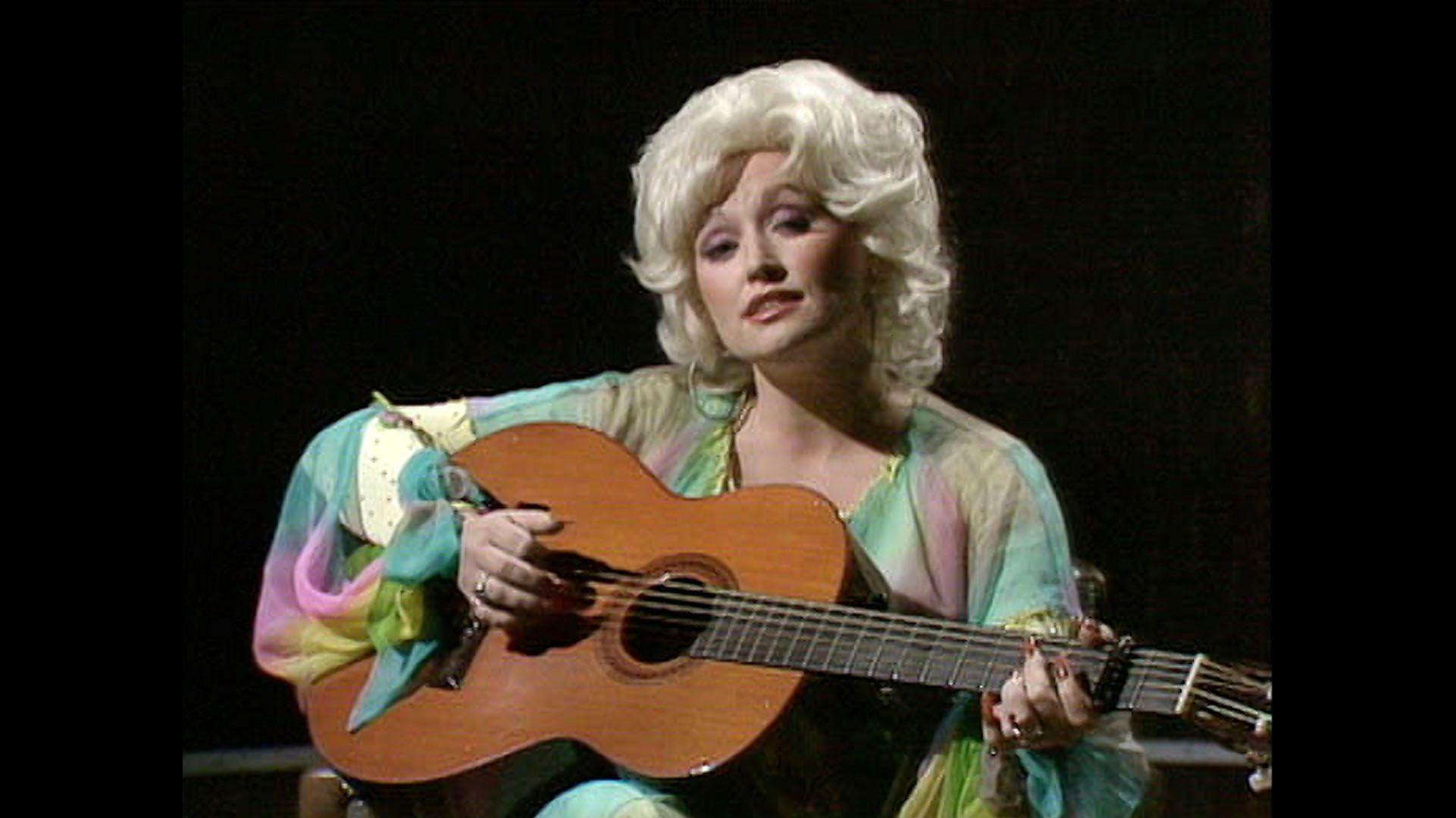 Una joven Dolly Parton tocando una guitarra acústica.