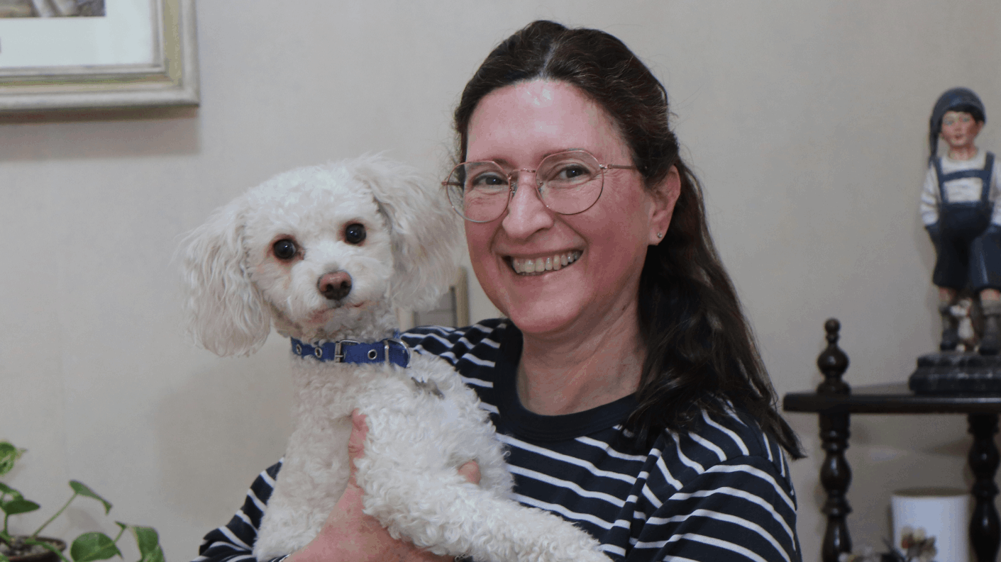 Retrato de Mónica Astorga sonriendo y sosteniendo a su perrito en su casa de Buenos Aires.