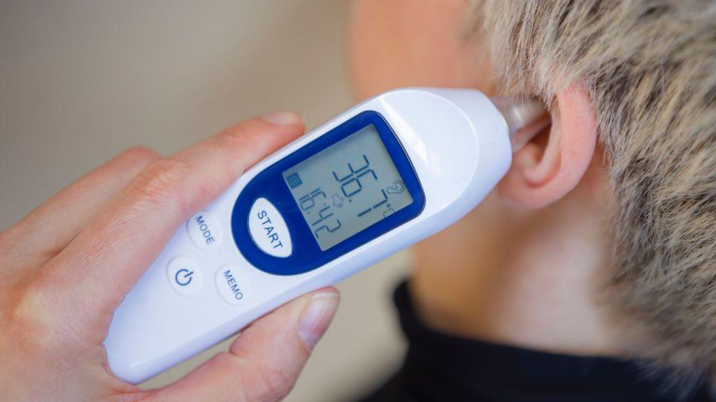 Una persona sostiene en su oreja un termómetro para medir la temperatura corportal