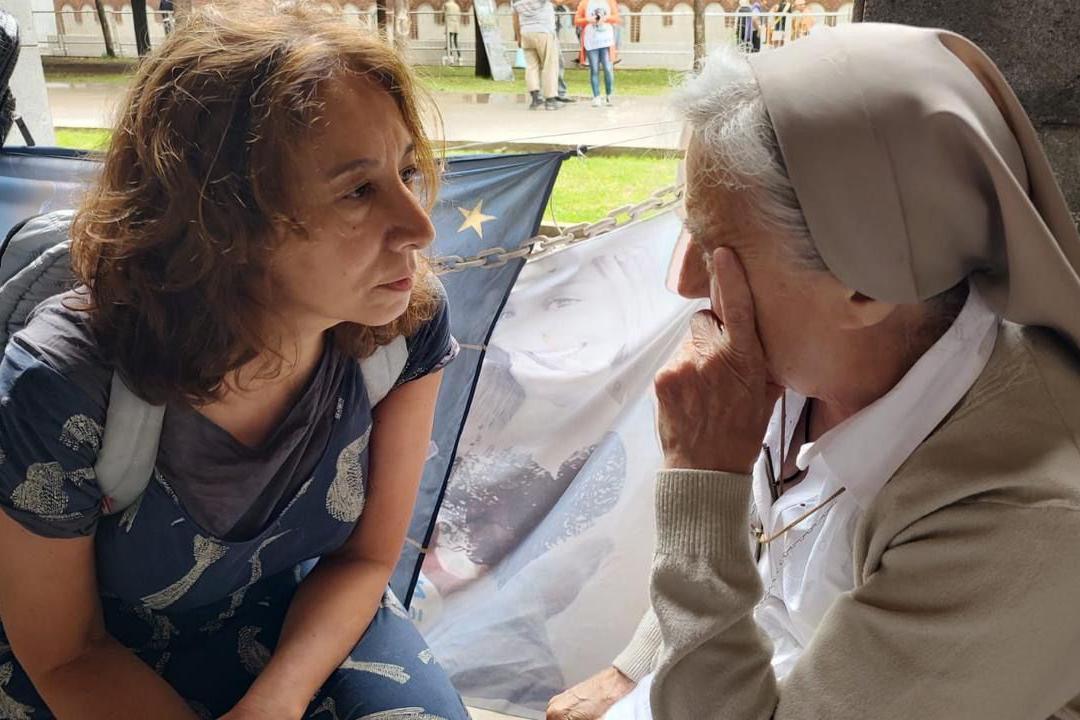 A la izquierda se ve a la periodista Liliana Viola con una camiseta de color azul. A la derecha, la monja Pelloni apoya su rostro en su mano izquierda. Lleva su hábito.